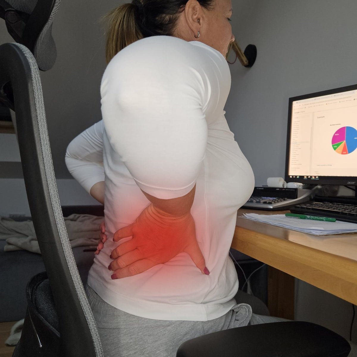 Woman at her desk pressing a hand on her aching lower back